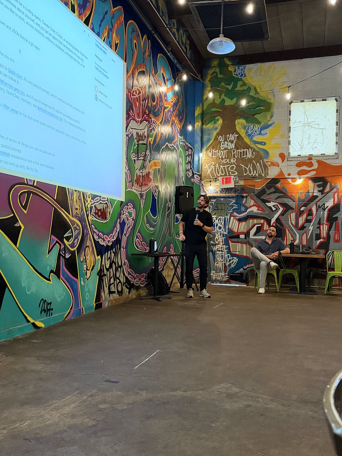 Alex presenting in front of Root Down's “put your roots down” mural
